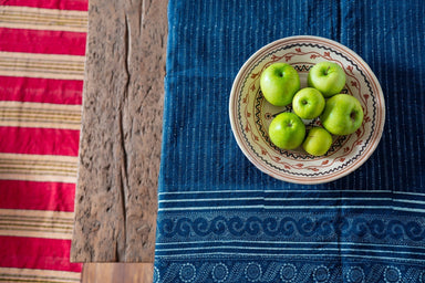 Antique handwoven Hungarian hemp table cloth with indigo wax resist pattern, featuring a ceramic bowl with green apples on a rustic wooden table.