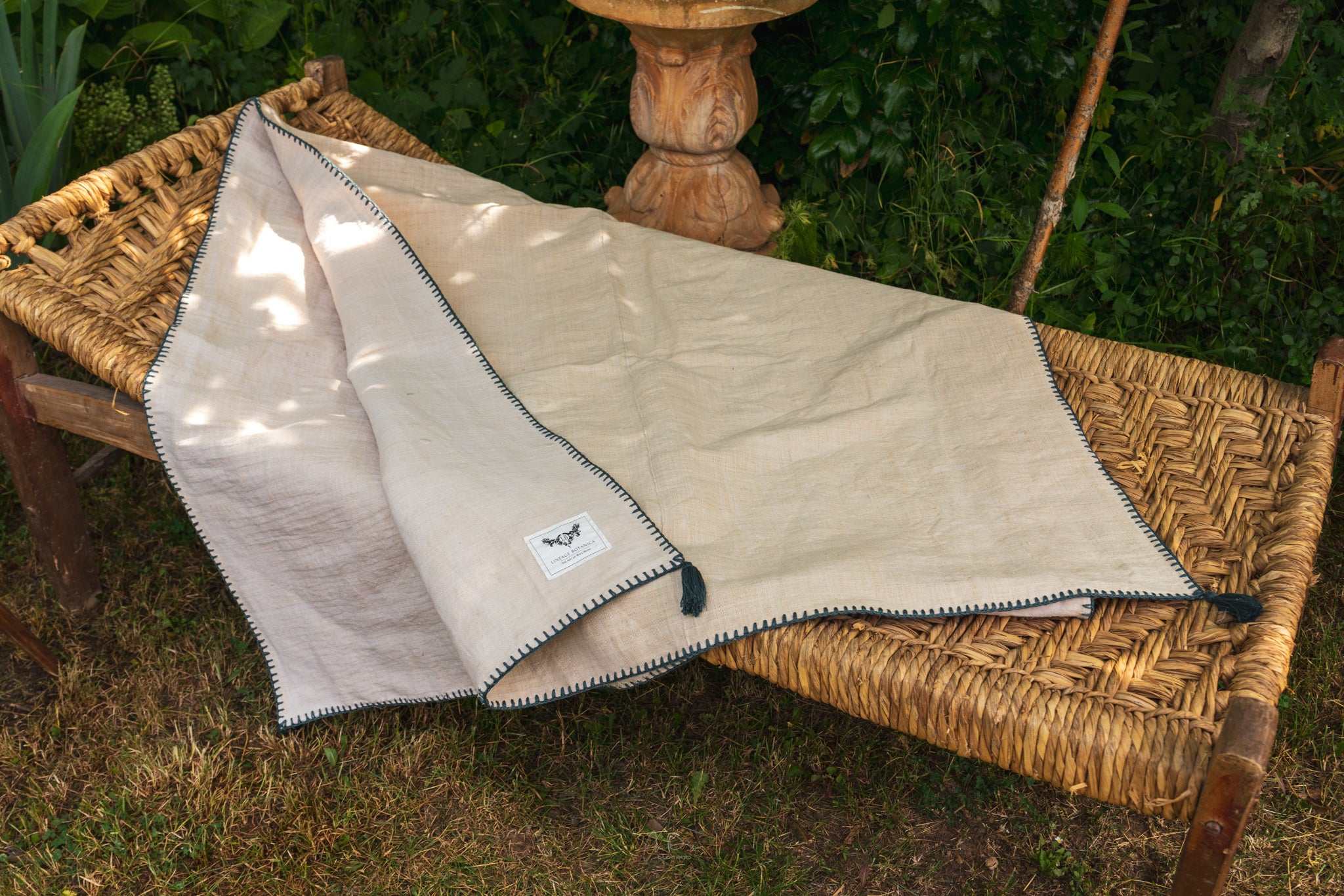 Organic handwoven antique hemp bed cover with indigo trim and tassels on a woven bench.
