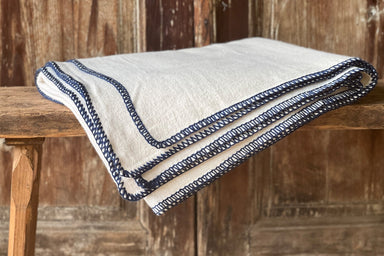Organic eco-cotton blanket with indigo trim on wooden surface.