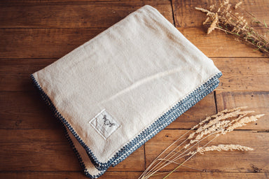 Organic eco-cotton blanket with indigo trim, artisan-crafted, on a wooden surface.