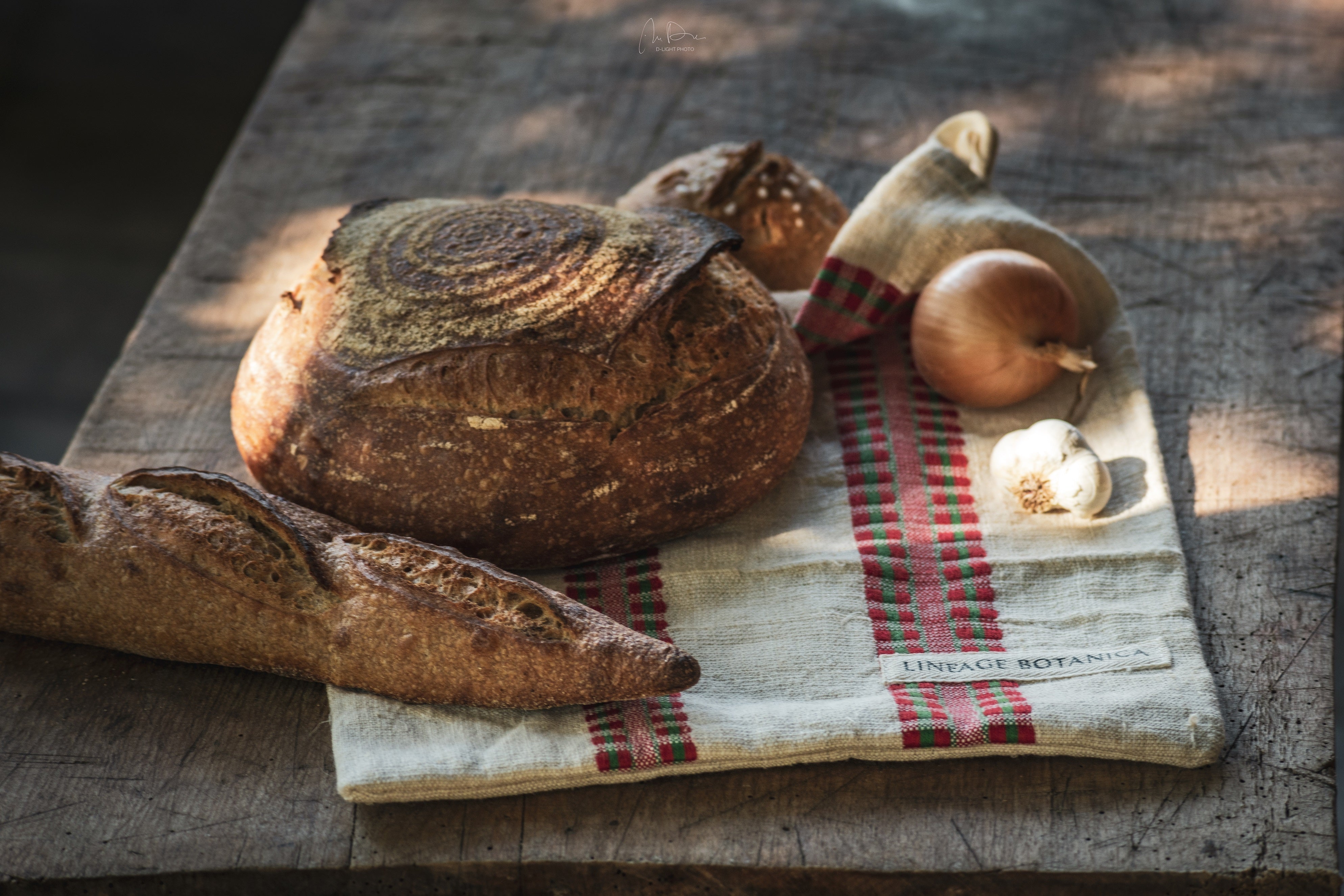 Handwoven antique hemp bread bag with rustic bread loaf and vegetables on wooden table.