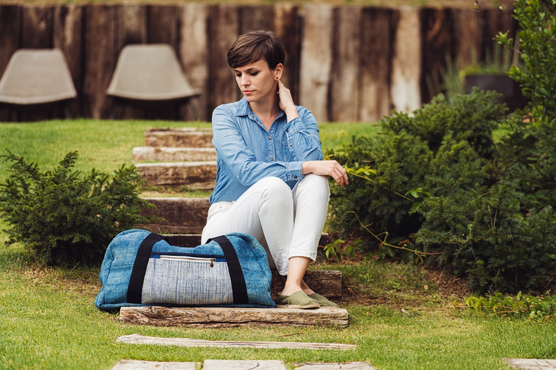 Handwoven hemp bag from antique grain sack with indigo hue and cotton straps placed outdoors beside a seated person.