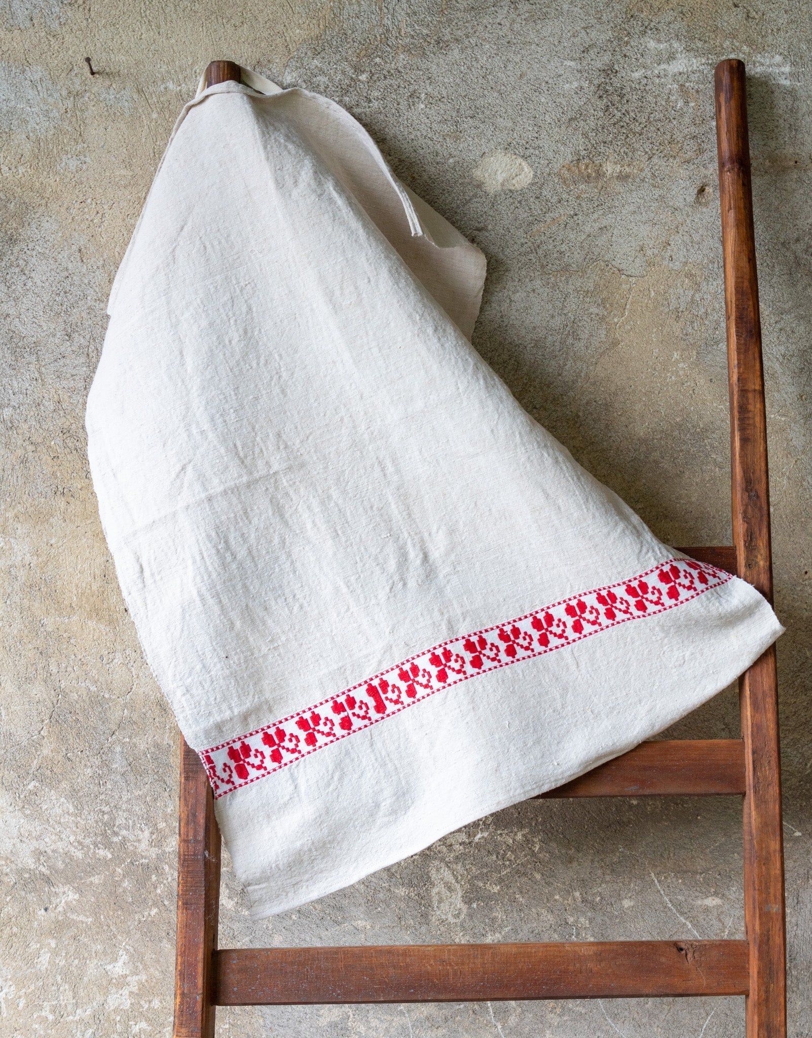 Handwoven antique Hungarian hemp towel with a red patterned border hanging on a wooden ladder.