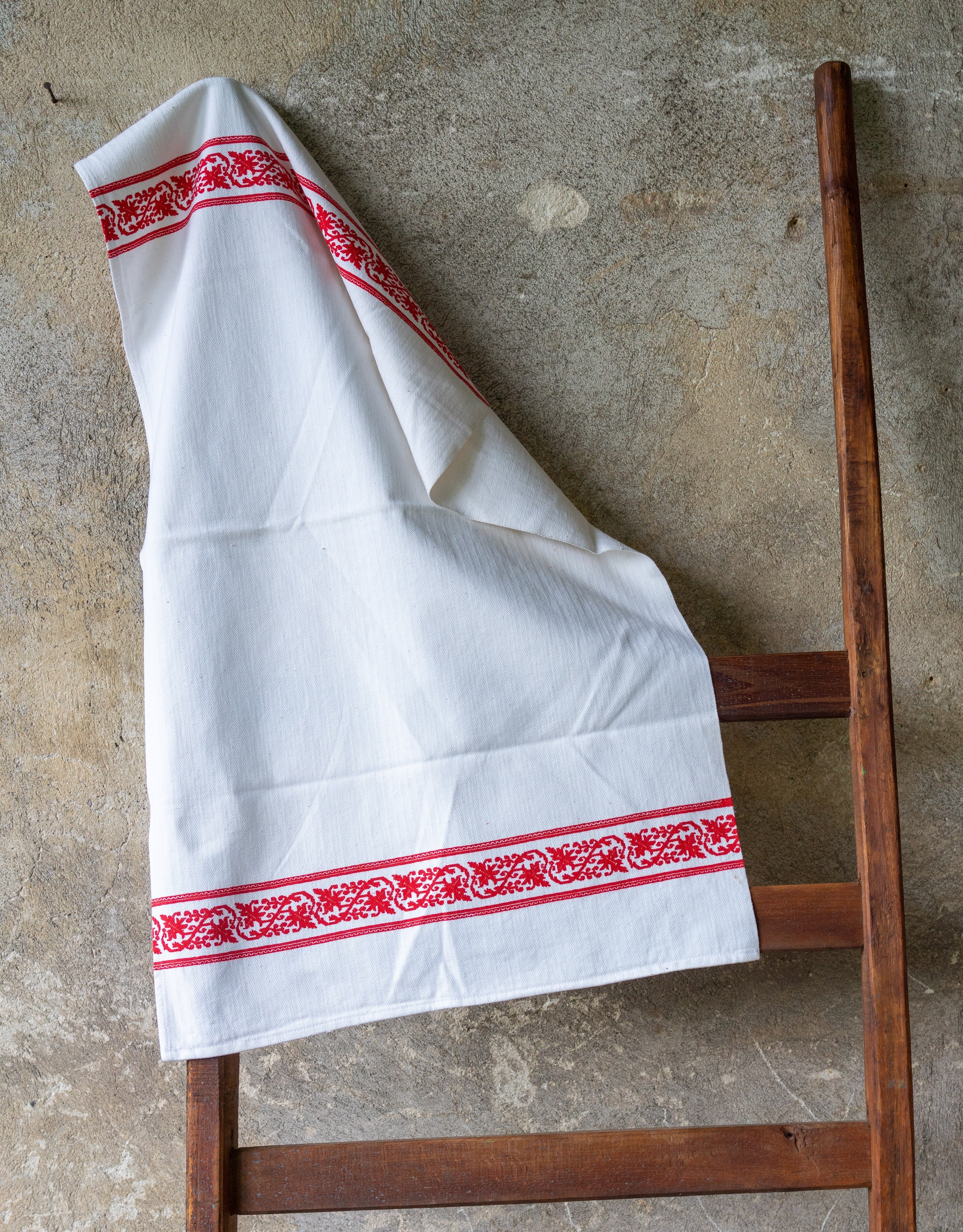 Handwoven antique Hungarian cotton towel with red accents hanging on a wooden ladder.