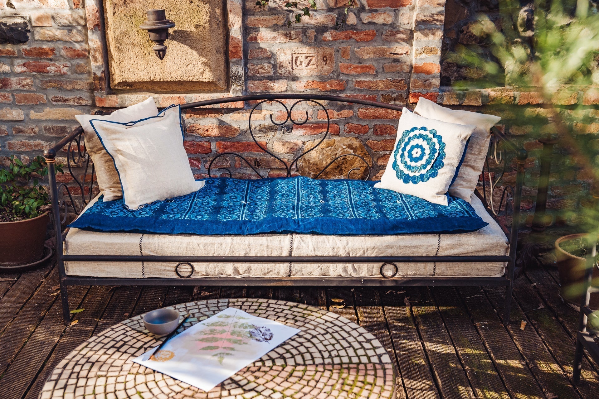 Handcrafted bedroll with antique hemp and indigo pattern on a metal daybed, surrounded by decorative pillows.