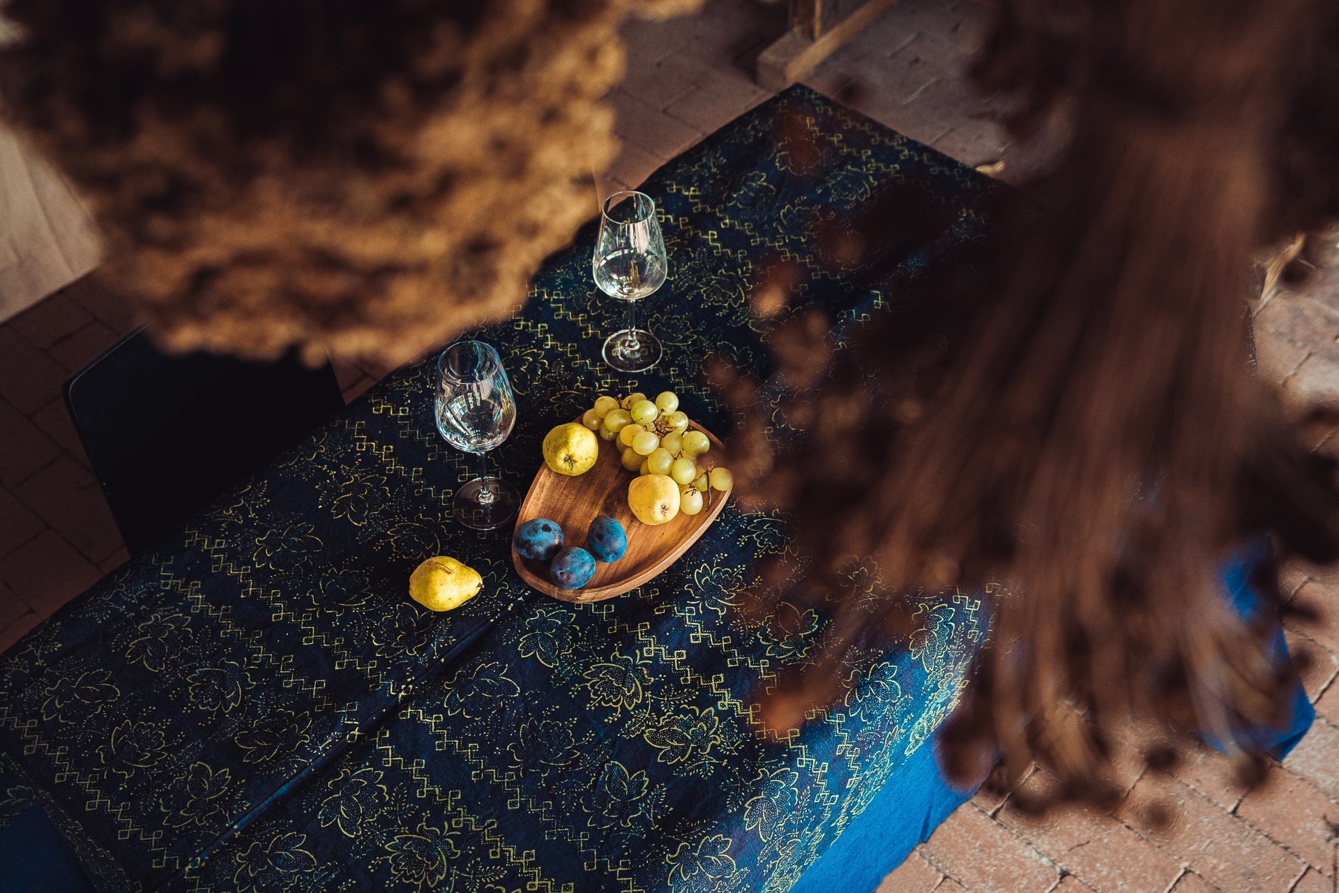 Antique handwoven Hungarian hemp table cloth with indigo dye and yellow pattern, adorned with fruits and wine glasses on a rustic table setting.