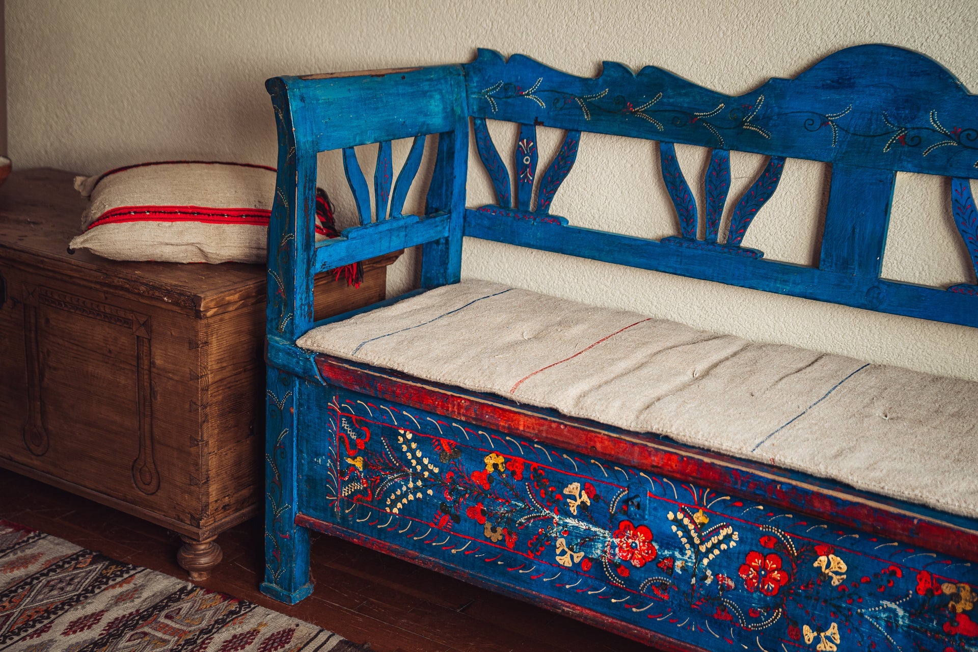 Antique handwoven hemp bedroll on blue wooden bench with floral design.