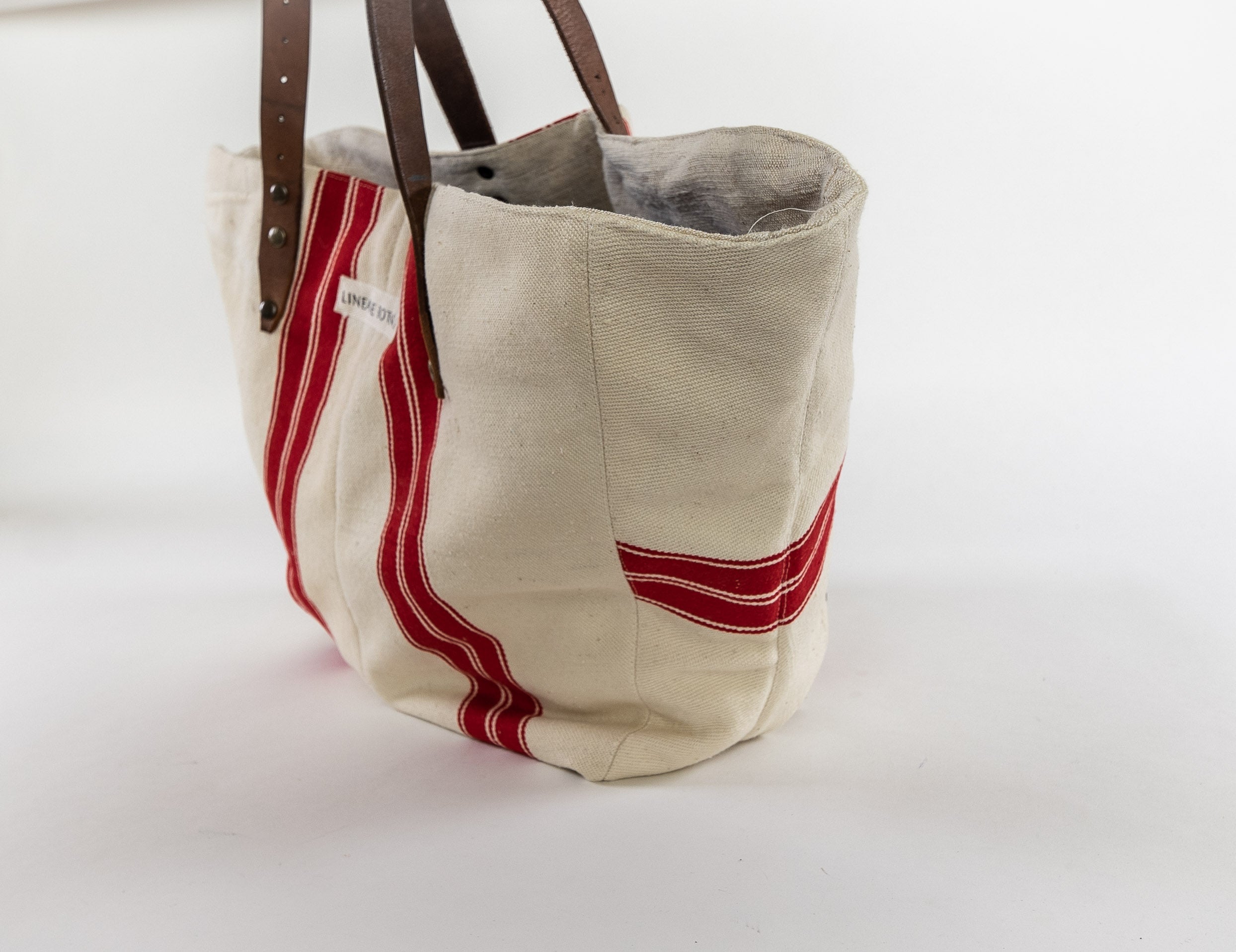 Handwoven antique Hungarian hemp bag with red stripes and brown leather handles.