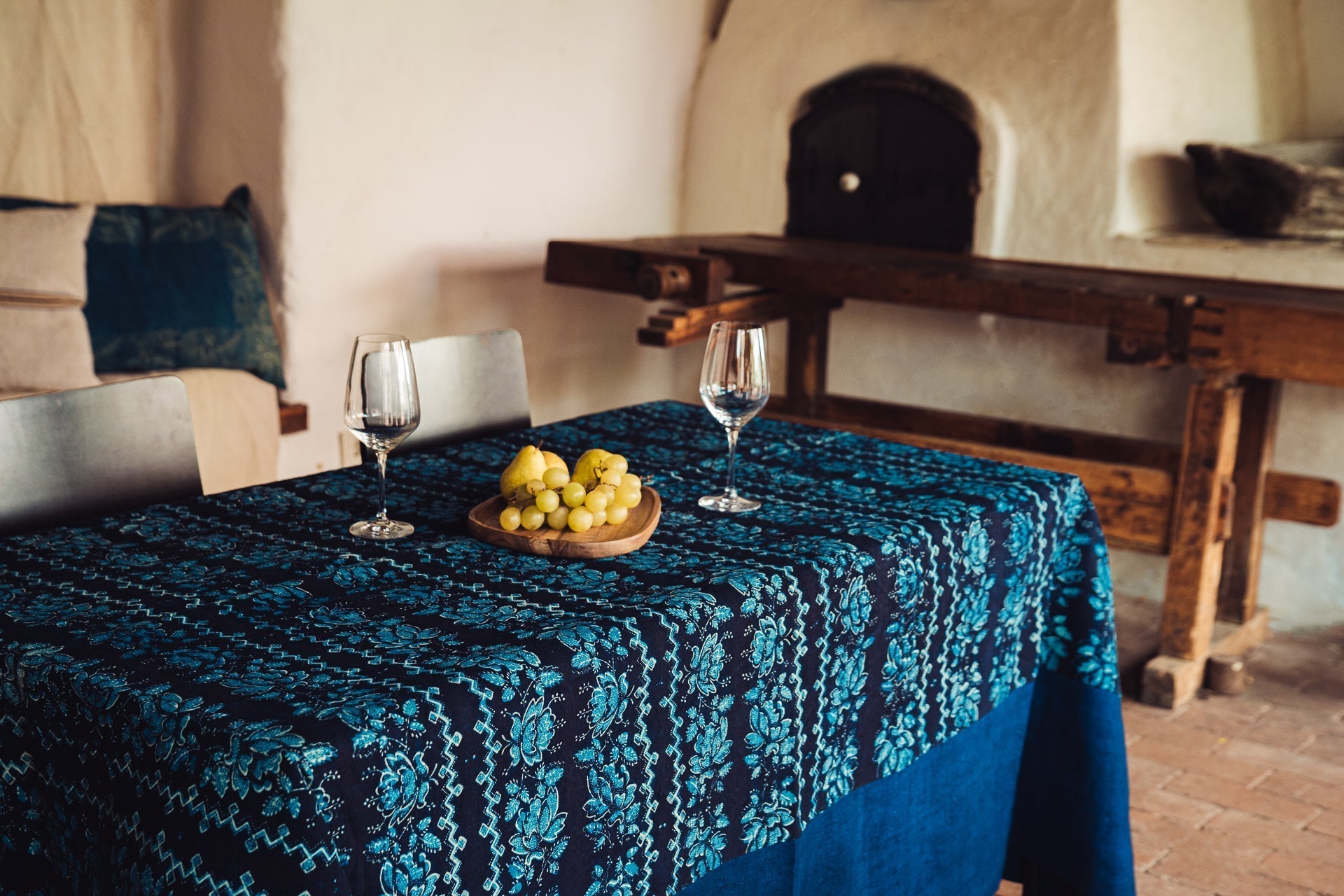 Antique handwoven Hungarian hemp table cloth with indigo wax resist dye and border, set on a dining table with two wine glasses and grapes.