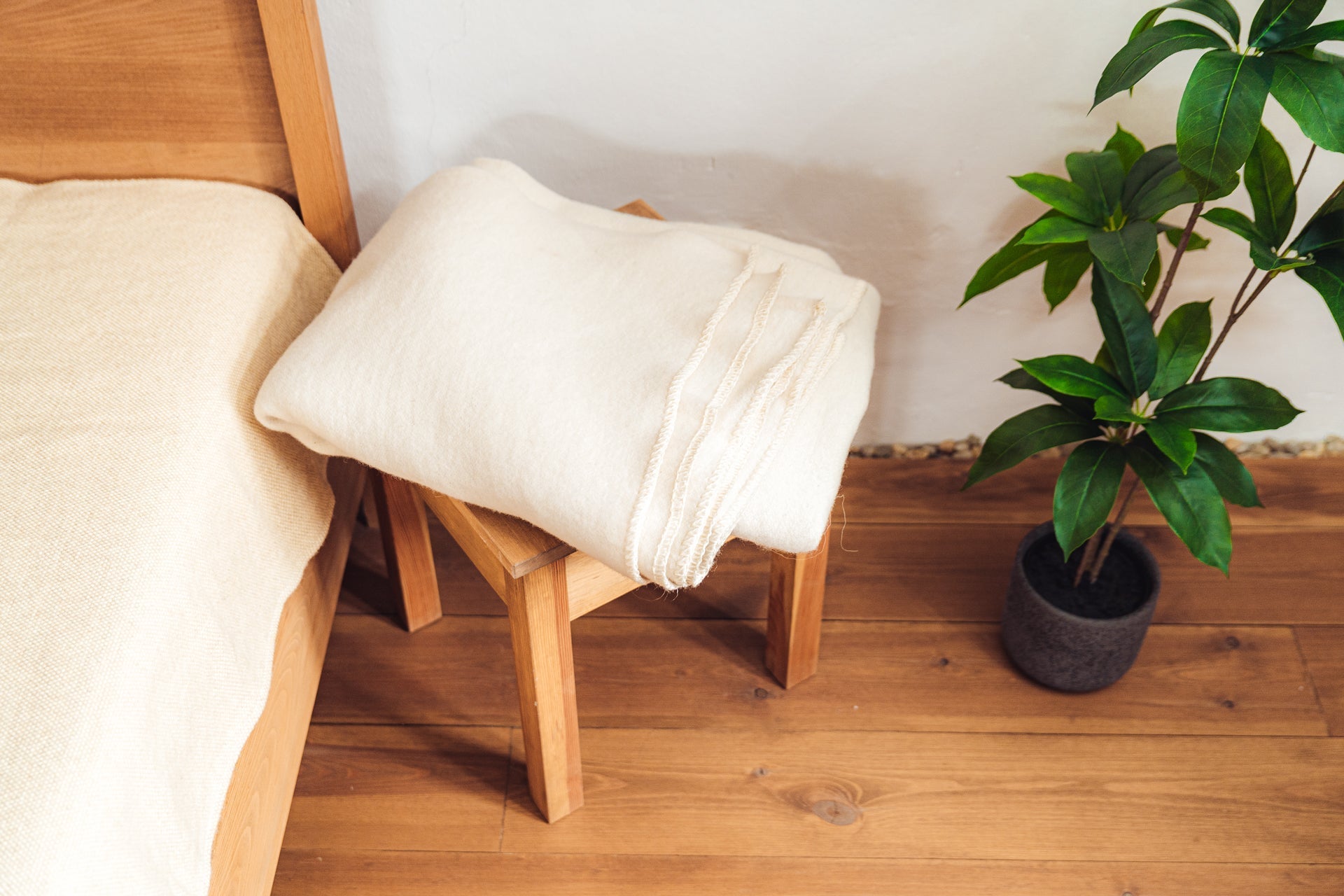 Handwoven Merino wool throw on wooden stool next to bed and plant.