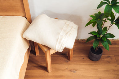 Handwoven Merino wool throw on wooden stool next to bed and plant.