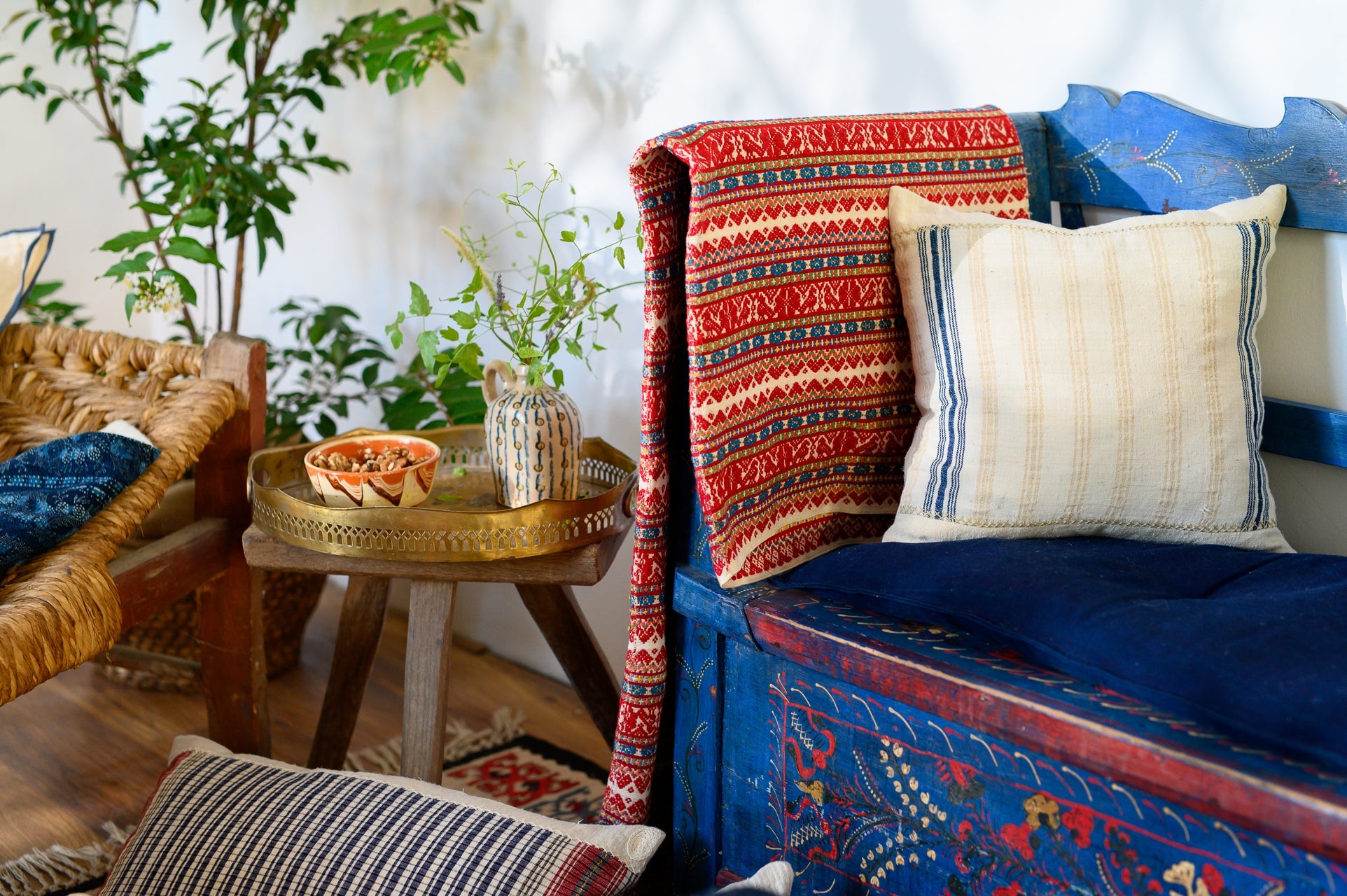 Handwoven antique hemp pillow on an intricately decorated blue bench with red patterned blanket in cozy home setting.