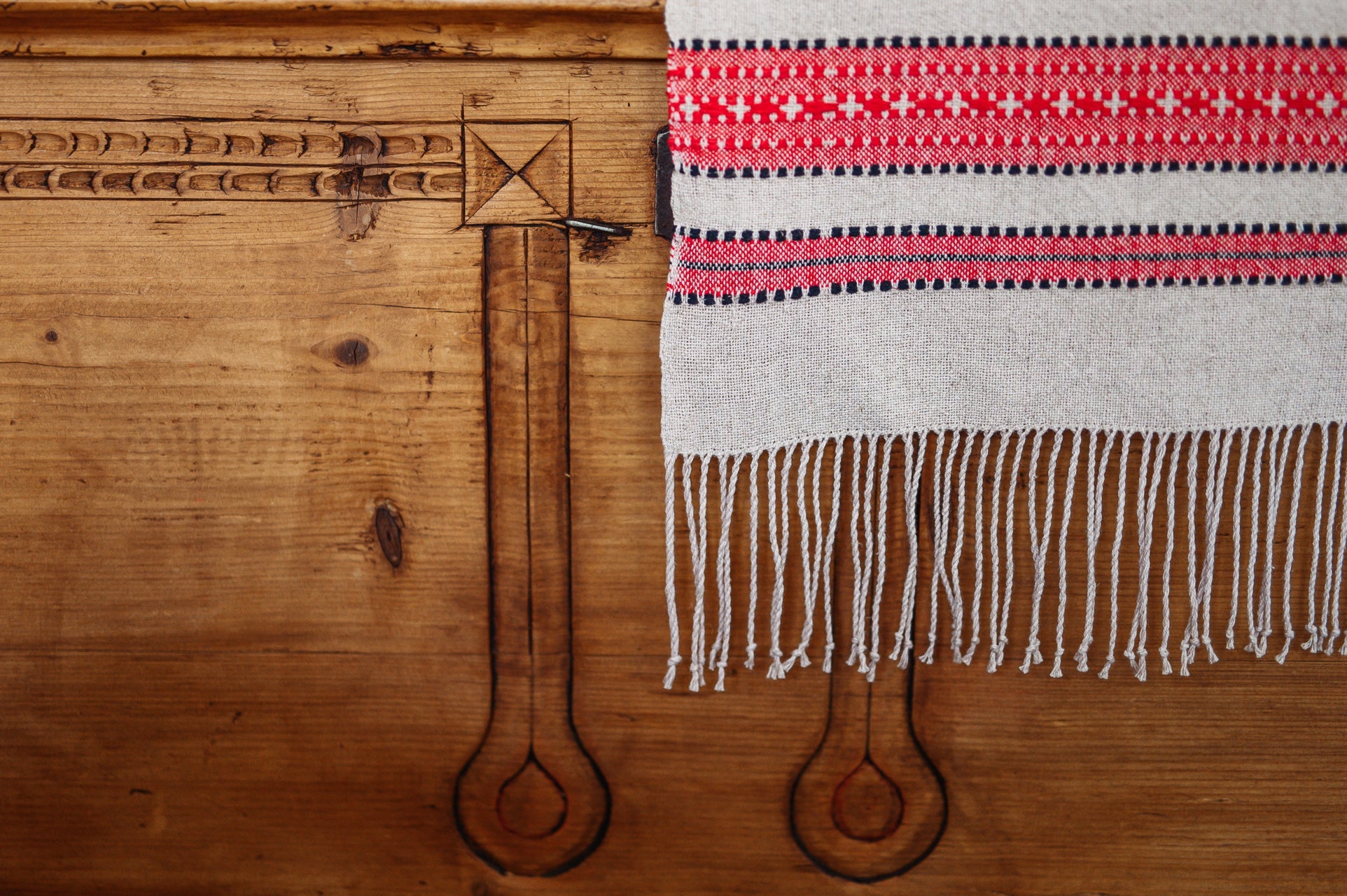 Organic handwoven hemp bed cover with red and black pattern and fringed edges.