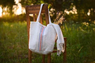 Antique grainsack bag made from handwoven organic hemp with re-used stitched straps, displayed on a chair in a natural setting.