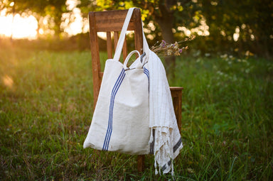 Antique grainsack bag from Hungary with blue stripes, handcrafted from vintage hemp, hanging on a wooden chair in a grassy field.