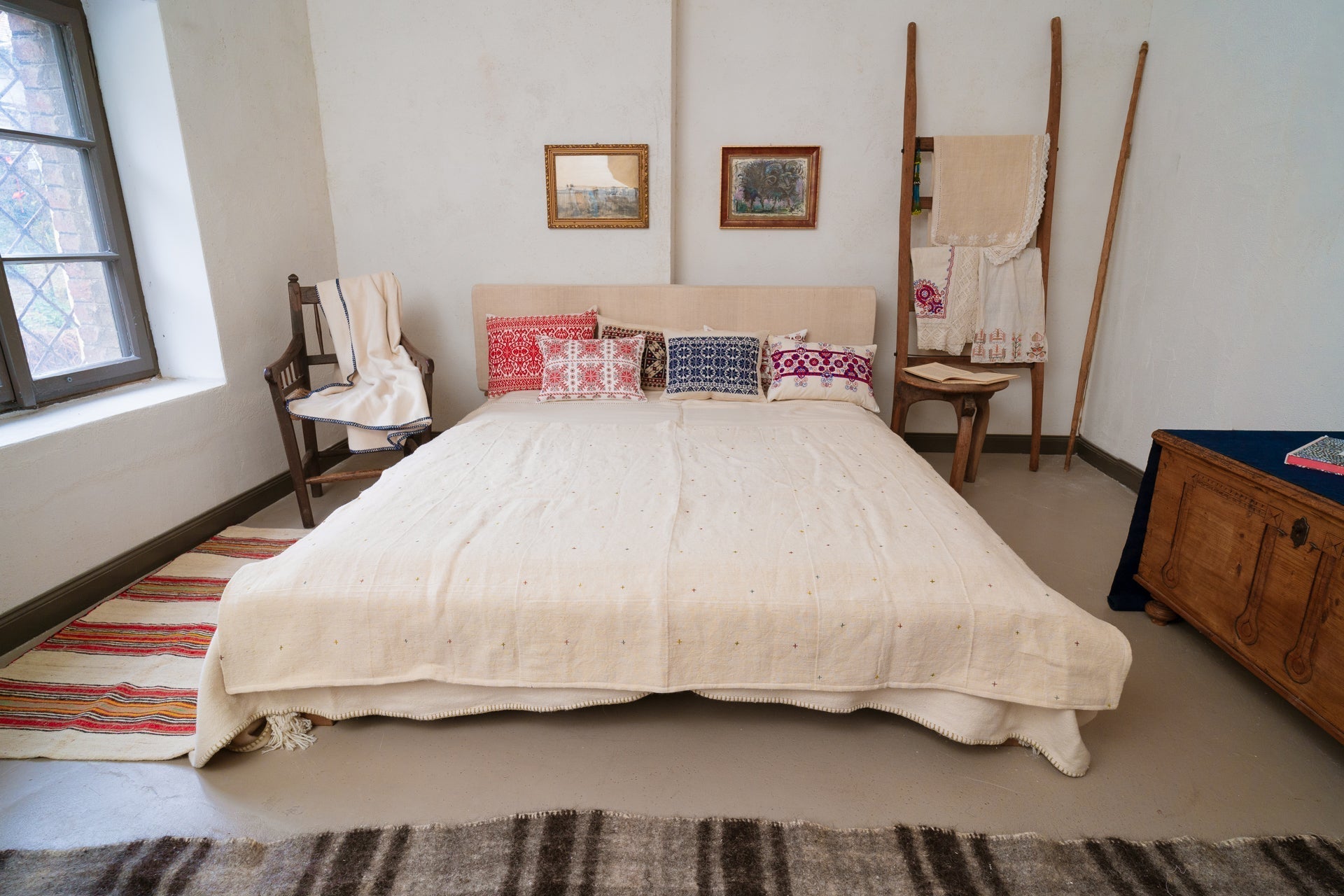 Embroidered handwoven antique Hungarian hemp pillow on bed with colorful cushions.