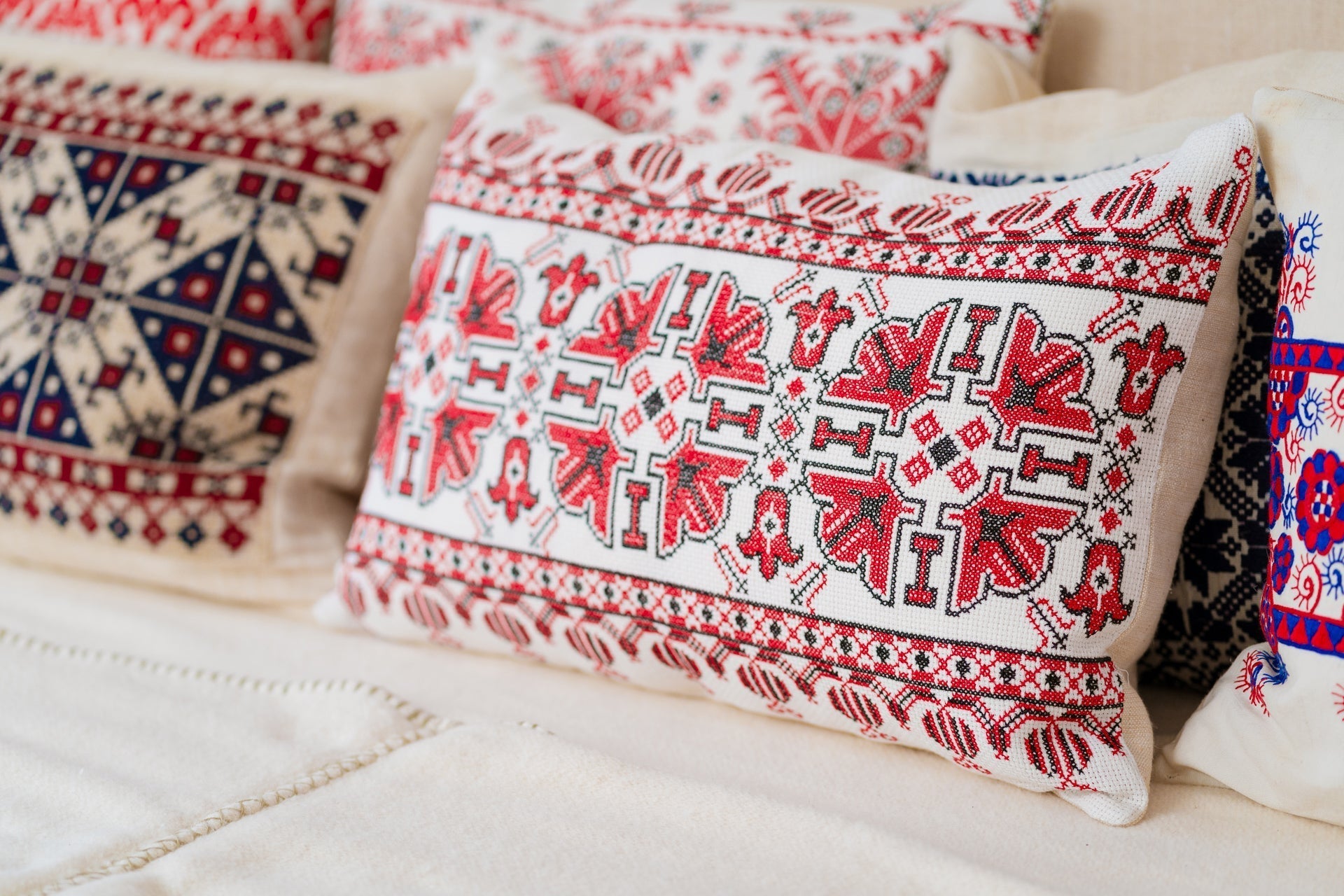 Embroidered handwoven antique Hungarian hemp pillow with intricate red and black patterns on a couch.