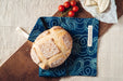 Handwoven antique hemp bread bag with over-dye indigo design, holding fresh bread on a wooden surface.