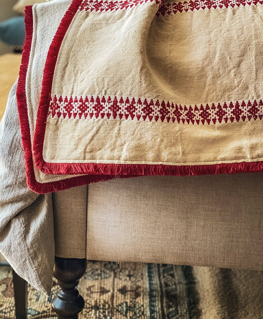Antique Hungarian hemp throw with red geometric patterns and eco-cotton backing draped over beige furniture