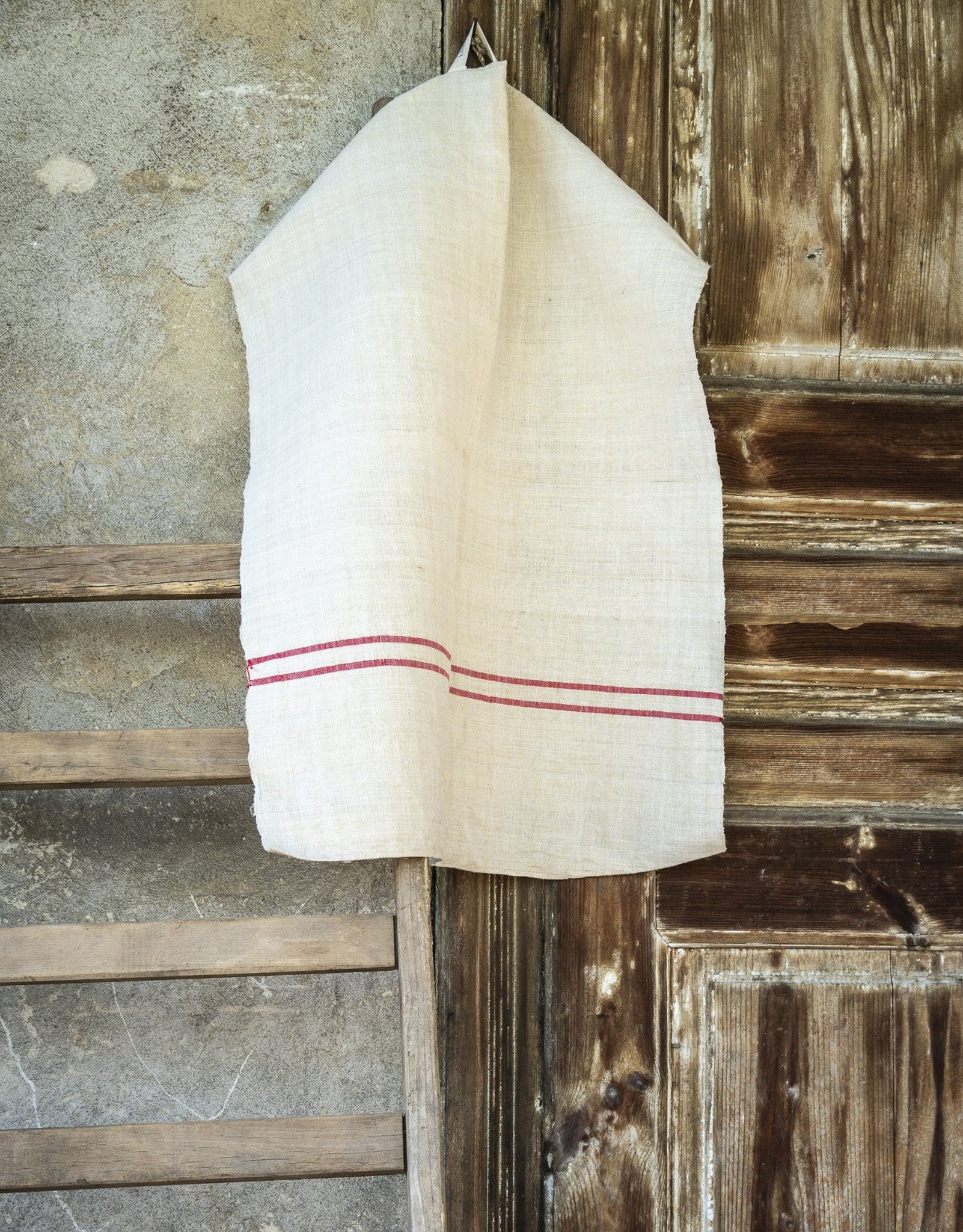 Handwoven antique Hungarian hemp towel, lightweight and absorbent, hanging against rustic wooden background.