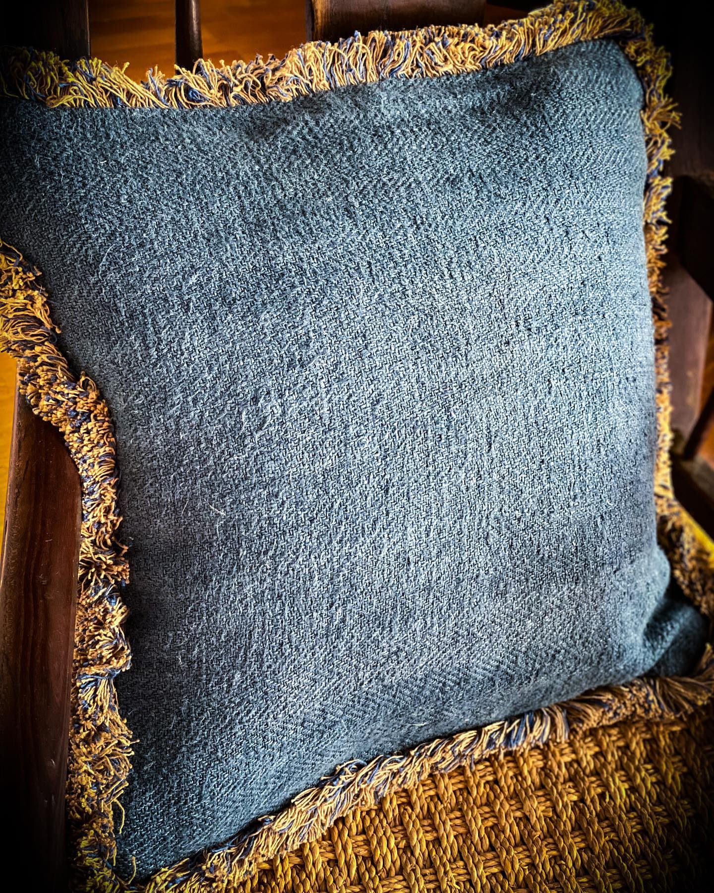 Antique Hungarian handwoven hemp pillow with rustic fringe detailing on a wooden chair.