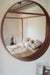 Antique Hungarian handwoven hemp pillow on bed with wooden frame reflected in round mirror.