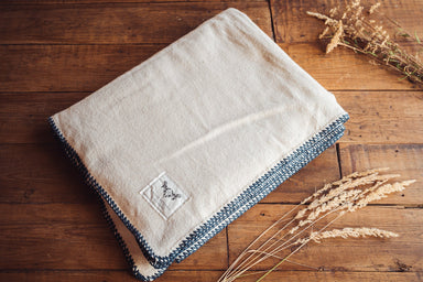 Organic eco-cotton blanket with indigo trim, hand-stitched detailing, on a wooden surface.