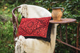 Antique handwoven Hungarian wool pillow with intricate red and black design on a rustic chair.