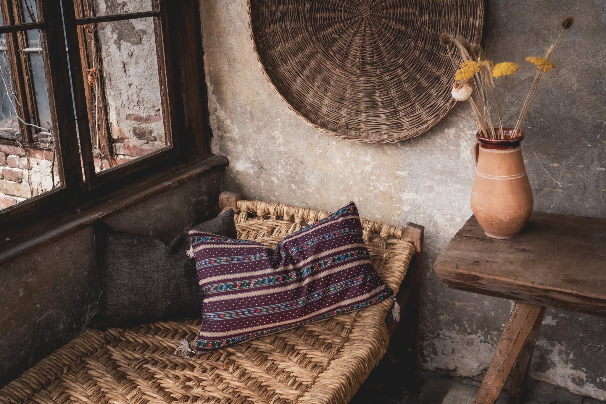 Handwoven Romanian artifact textile pillow on rustic woven bench.