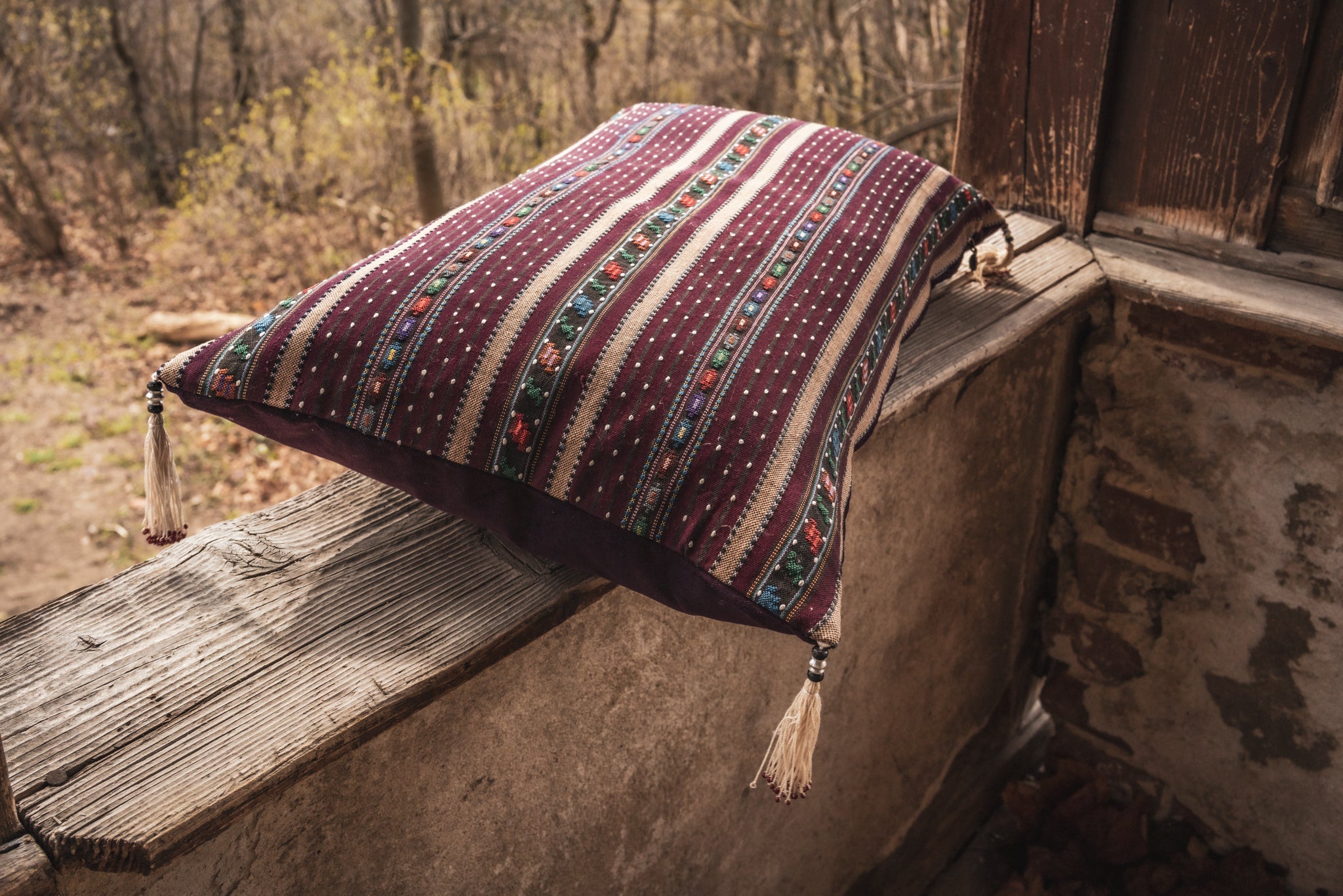 Handwoven Romanian artifact textile pillow with tassels in rustic setting.