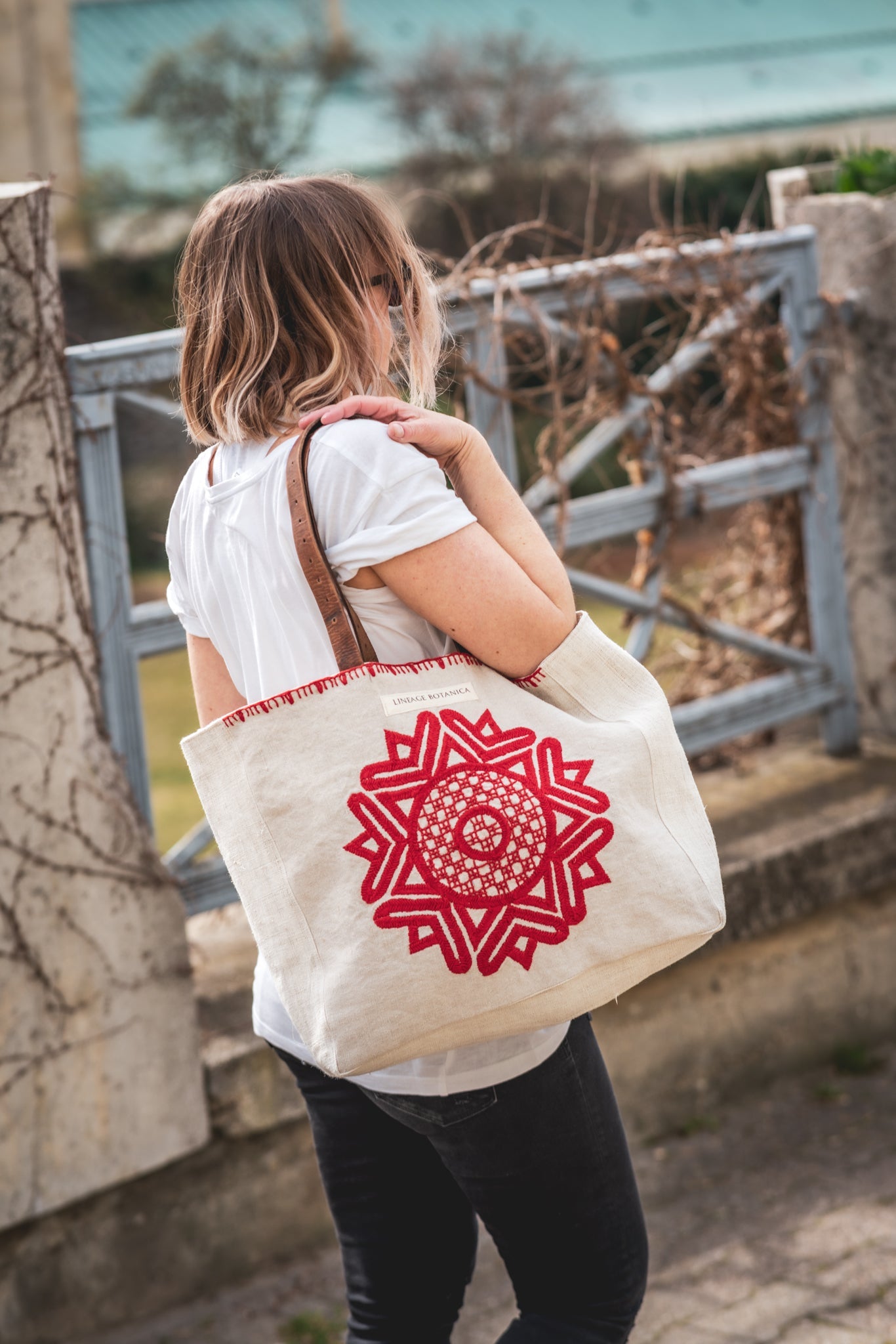 Handwoven antique hemp grain sack bag with red embroidered Mandala and recycled leather strap.