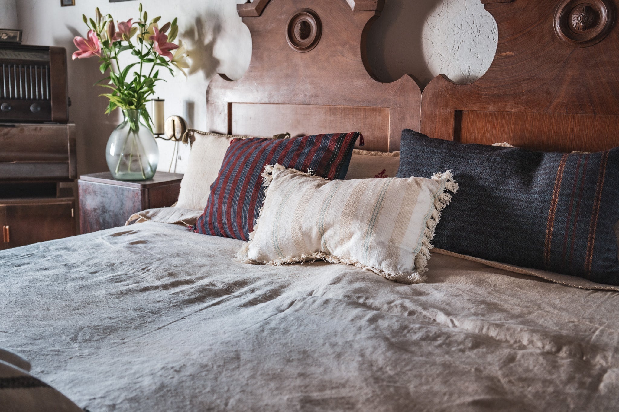 Antique handwoven decorative pillows on elegant bed with wooden headboard.