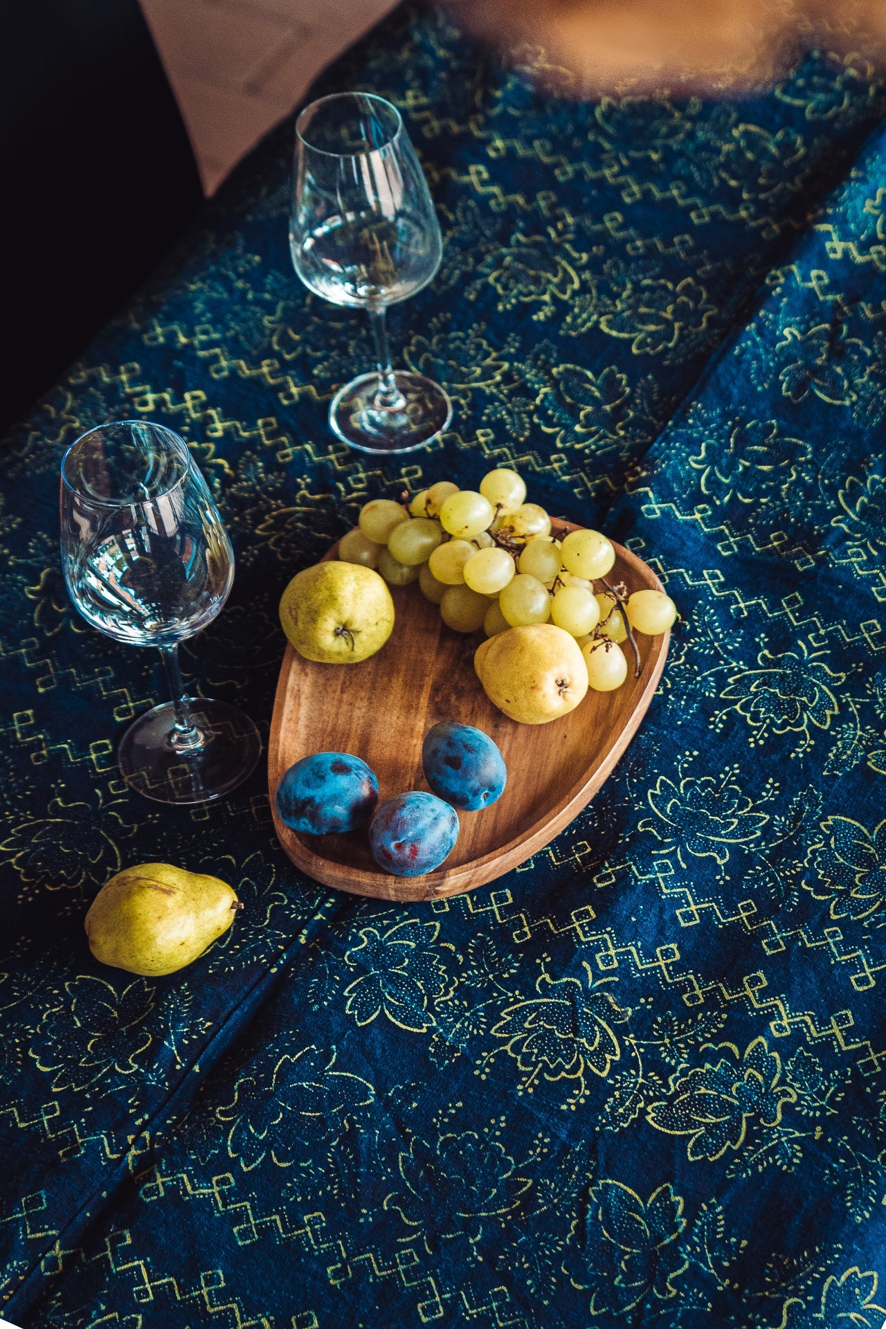 Antique handwoven Hungarian hemp table cloth with indigo dye and yellow pattern, displayed with fruits and wine glasses.