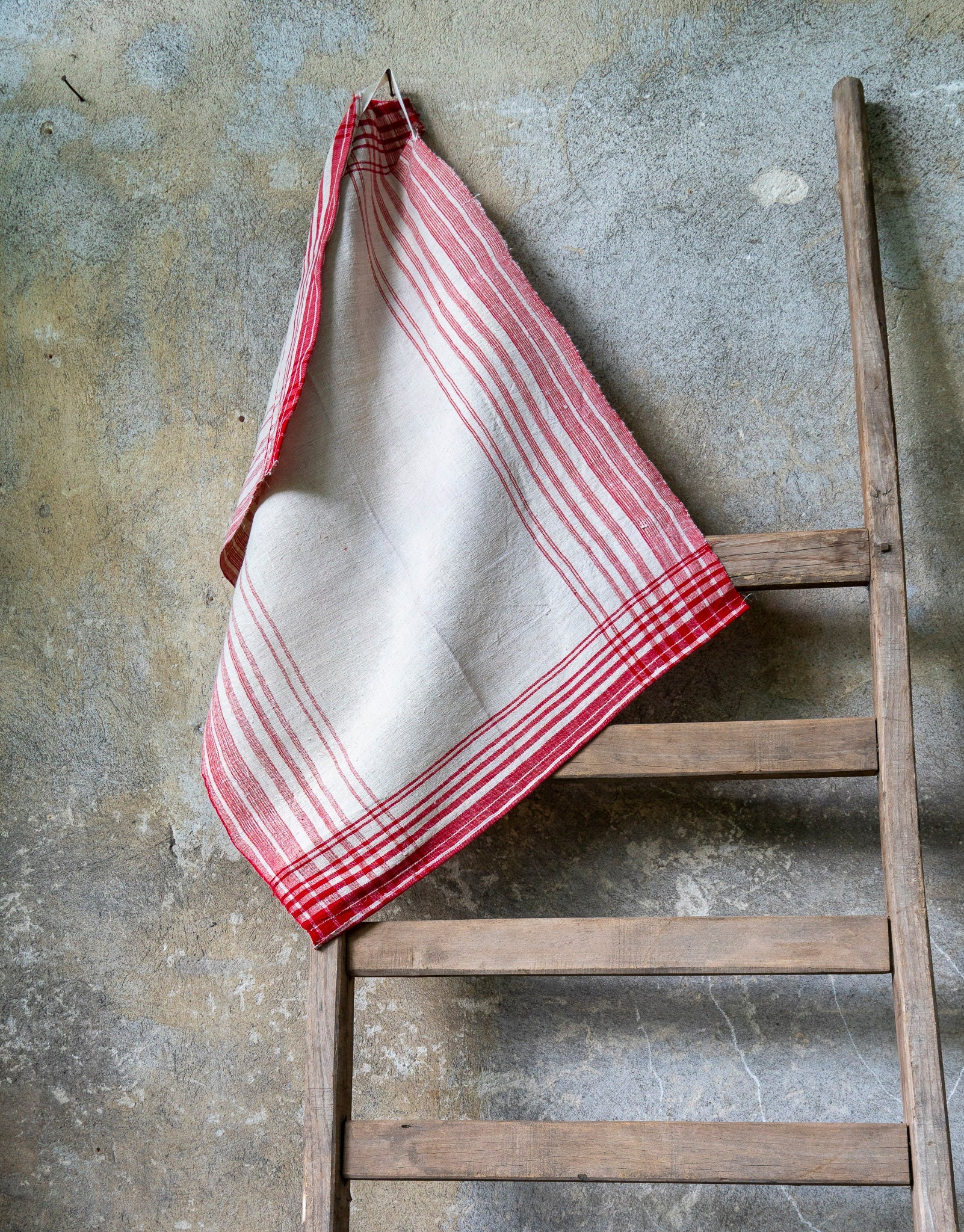 Handwoven antique Hungarian hemp towel hanging on a rustic wooden ladder.