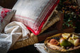 Antique handwoven decorative pillow with red stripes on a rustic bench.