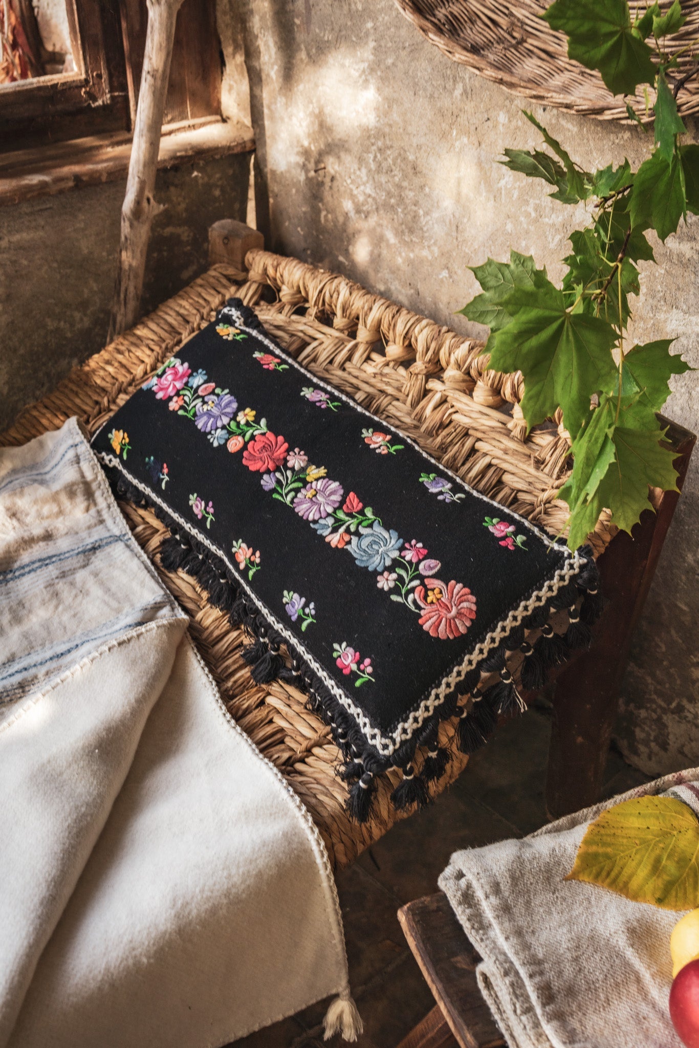 Embroidered handwoven antique Hungarian hemp pillow with cotton fringe and hemp back, displayed on a woven chair.