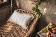Antique handwoven decorative pillow with cotton fringe on woven chair.