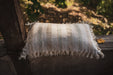 Antique handwoven decorative pillow with cotton fringe displayed outdoors.