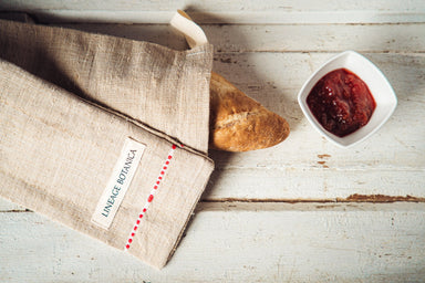 Handwoven antique and vintage hemp baguette bag with bread next to jam on rustic table.