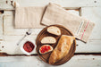 Handwoven antique hemp baguette bag with bread and jam on rustic table.