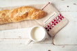 Handwoven antique and vintage hemp baguette bag with red embroidery, next to a baguette and a cup of milk on a rustic surface.