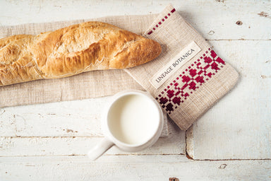 Handwoven antique and vintage hemp baguette bag with red embroidery, next to a baguette and a cup of milk on a rustic surface.