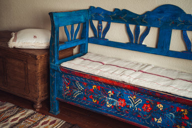 Antique handwoven hemp bedroll on decorative blue wooden bench with Hungarian grain sack design.