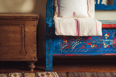 Antique handwoven hemp bedroll on colorful wooden bench.