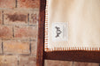 Eco-cotton throw in cinnamon with hand stitching on wooden chair.