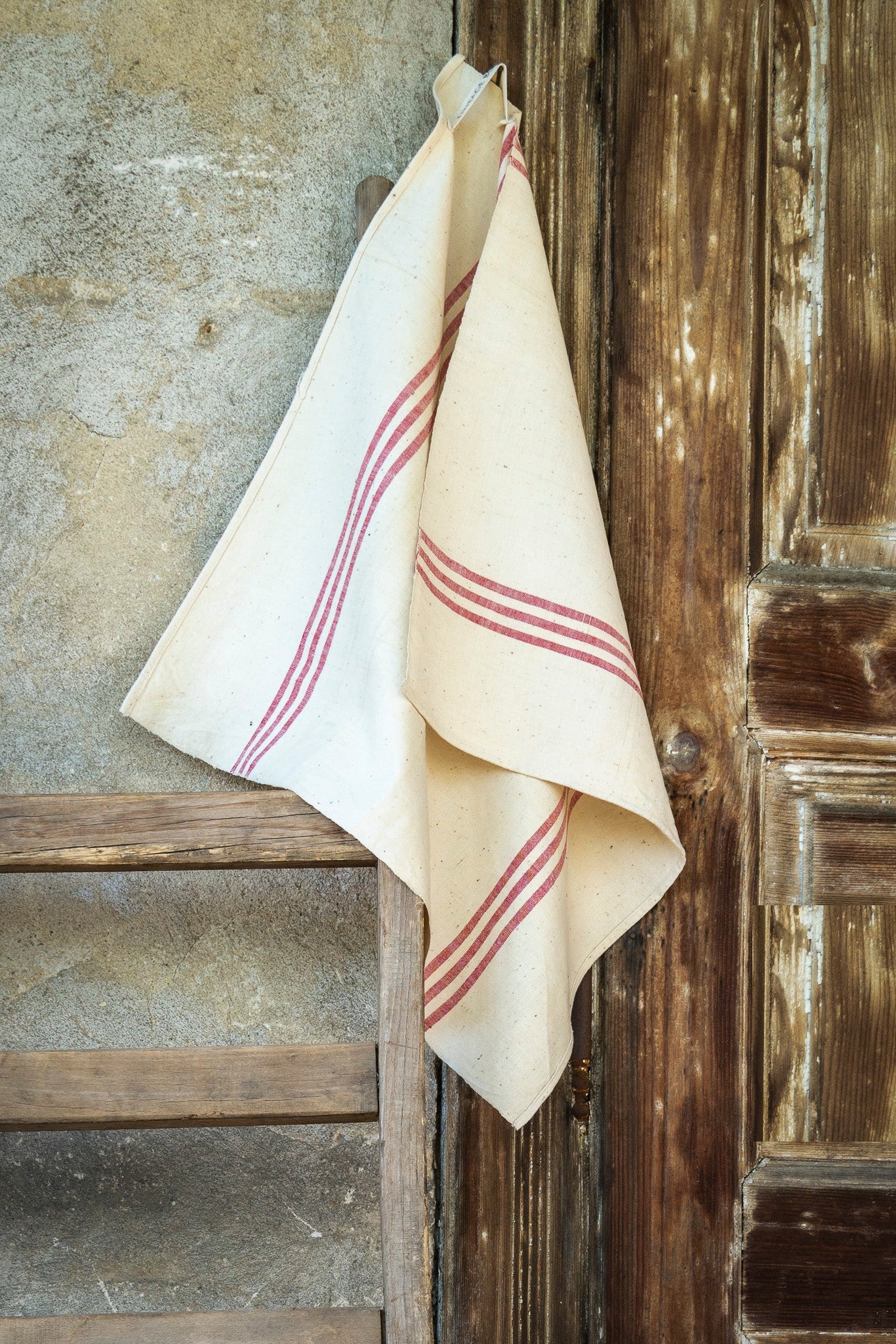 Handwoven antique Hungarian cotton towel with red stripes hanging against rustic wooden backdrop.