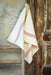 Handwoven antique Hungarian cotton towel with red stripes hanging against rustic wooden backdrop.